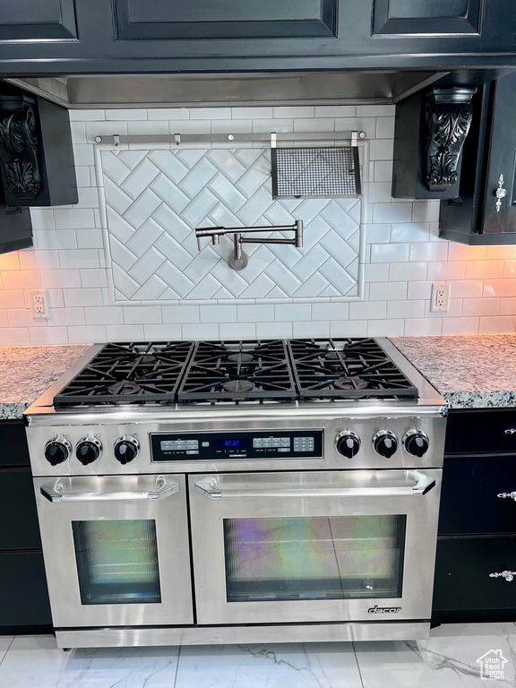 Kitchen featuring stainless steel range with gas cooktop, light marble finish flooring, decorative backsplash, dark cabinetry, and light stone counters