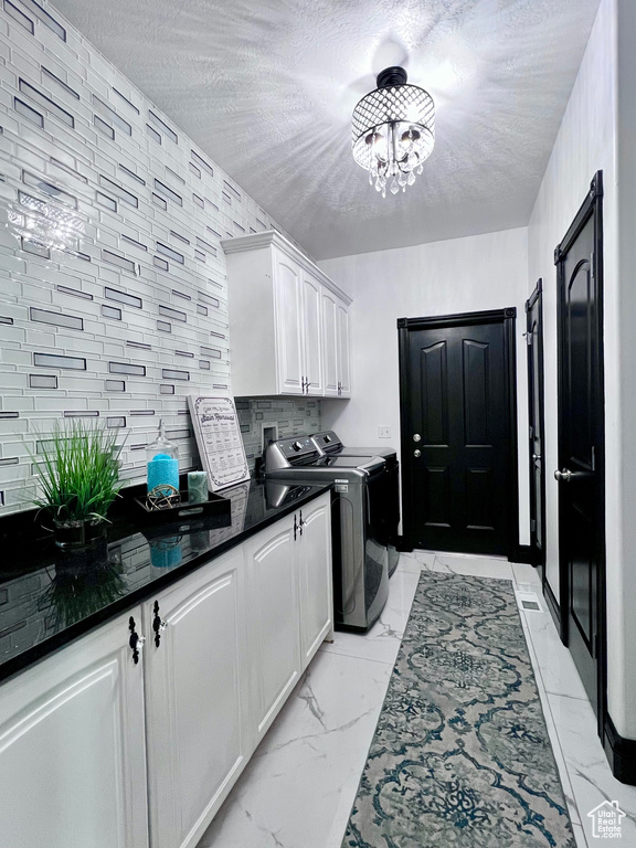 Washroom featuring cabinet space, light marble finish floors, independent washer and dryer, a chandelier, and a textured ceiling