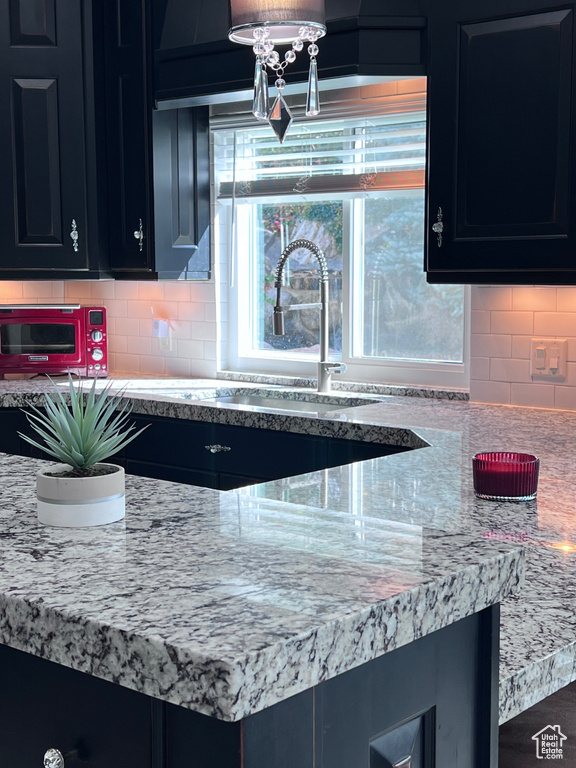 Kitchen with dark cabinets, backsplash, a sink, and light stone counters
