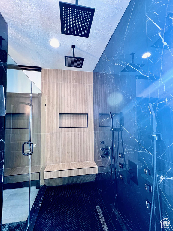 Bathroom with a shower stall, a textured ceiling, and tile walls