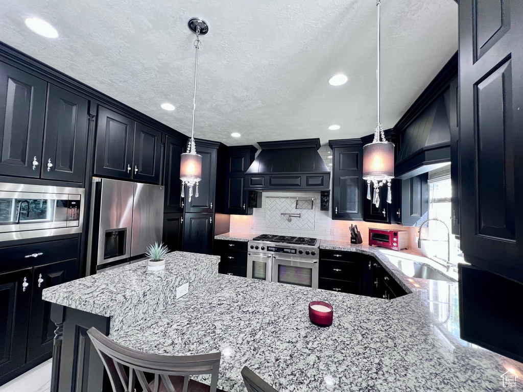 Kitchen featuring appliances with stainless steel finishes, a sink, light stone counters, backsplash, and dark cabinetry