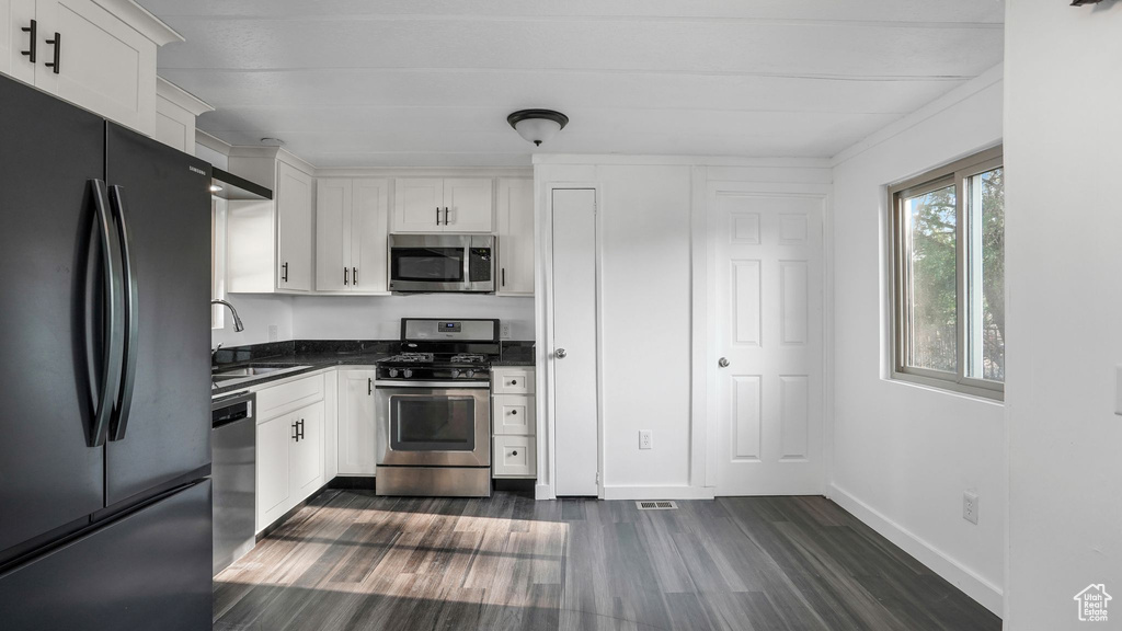 Kitchen featuring appliances with stainless steel finishes, a sink, dark wood finished floors, dark countertops, and white cabinetry