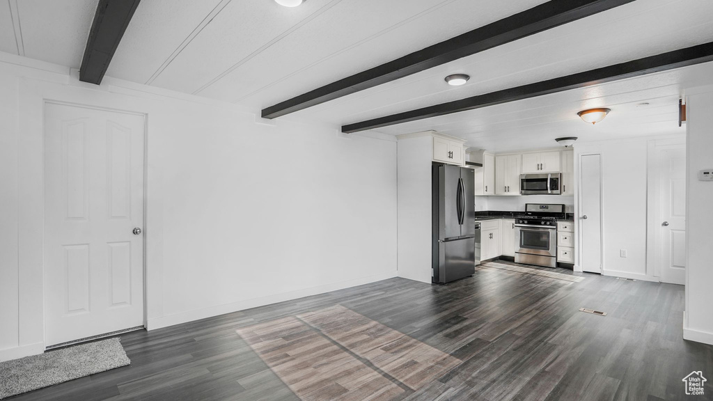 Unfurnished living room featuring beamed ceiling, dark wood-style floors, and baseboards