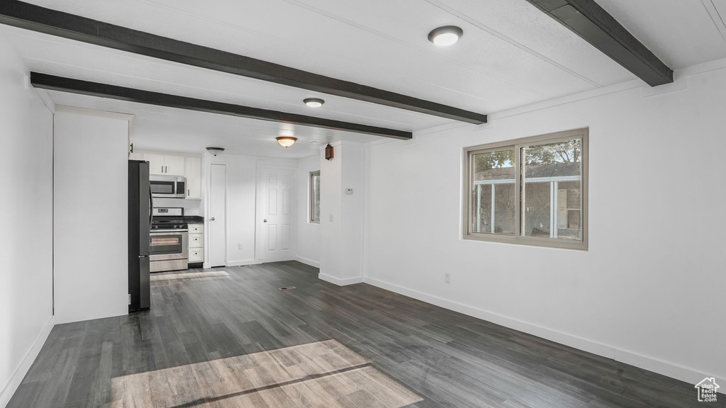 Unfurnished living room featuring beamed ceiling, baseboards, and dark wood-style floors