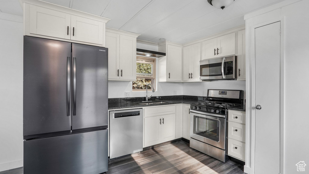 Kitchen featuring appliances with stainless steel finishes, a sink, dark wood finished floors, and white cabinetry