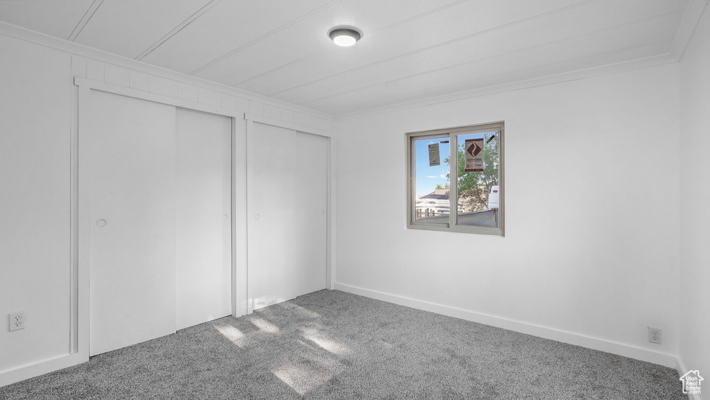Unfurnished bedroom featuring carpet flooring, two closets, and ornamental molding