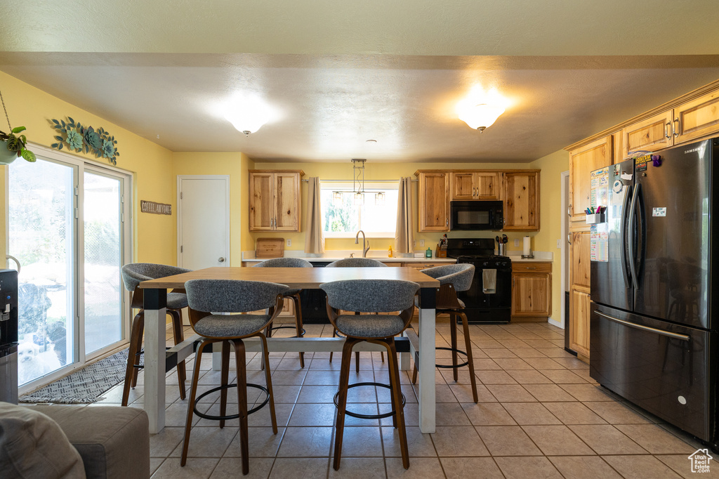 Kitchen featuring black appliances, light tile patterned floors, a sink, light countertops, and a breakfast bar