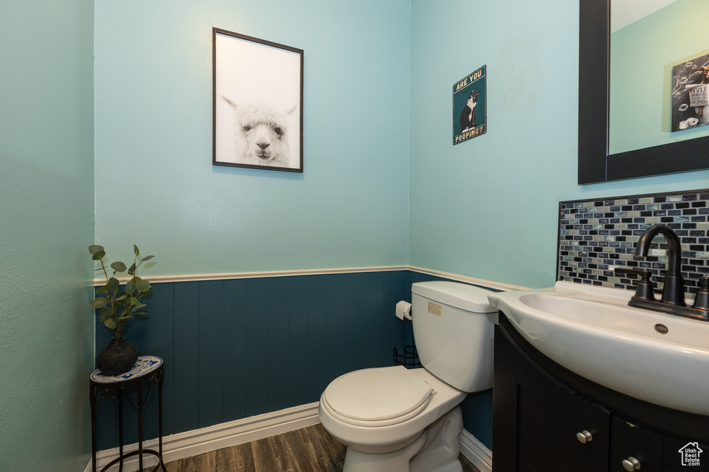 Bathroom featuring vanity, toilet, a wainscoted wall, wood finished floors, and decorative backsplash