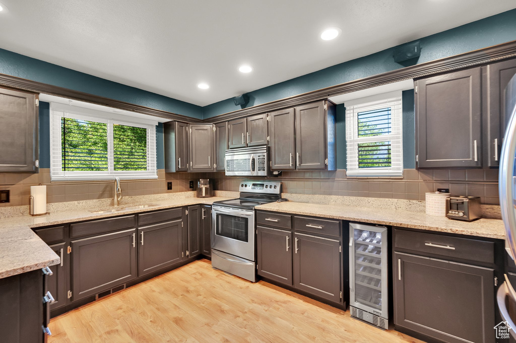 Kitchen featuring wine cooler, appliances with stainless steel finishes, a sink, decorative backsplash, and light wood-style floors