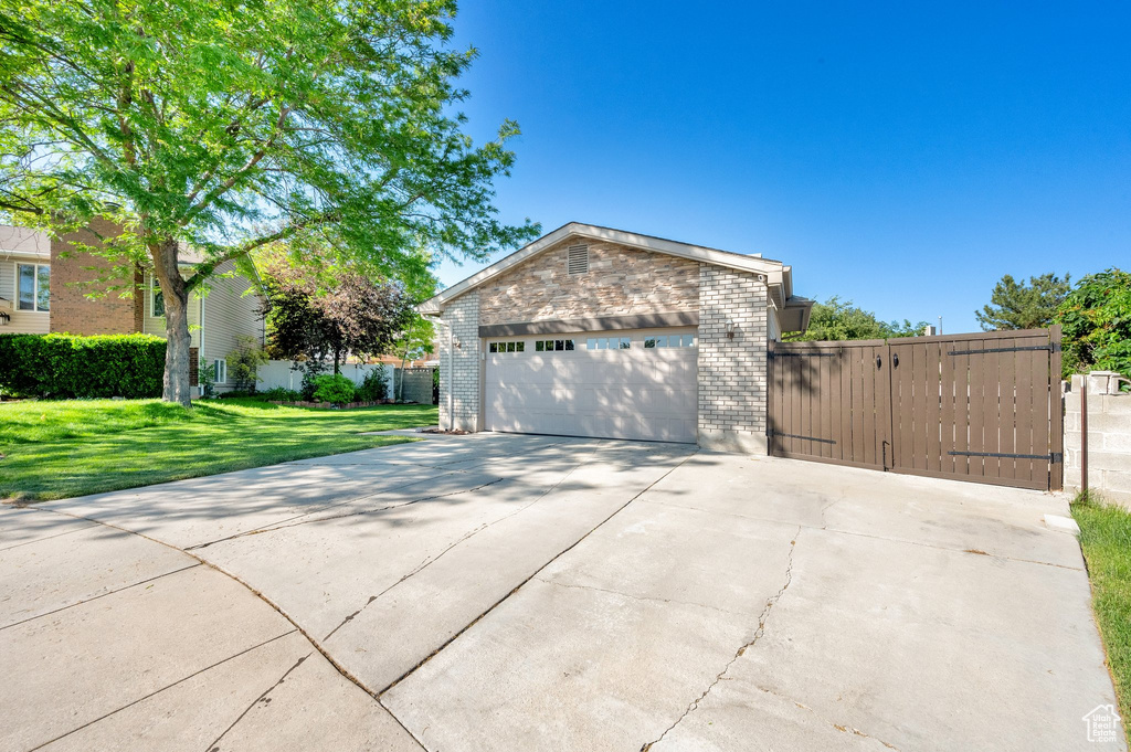 View of front facade with brick siding, a gate, driveway, and a garage