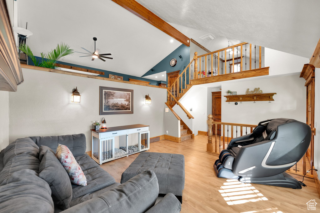 Living room with ceiling fan, high vaulted ceiling, beam ceiling, wood finished floors, and stairway