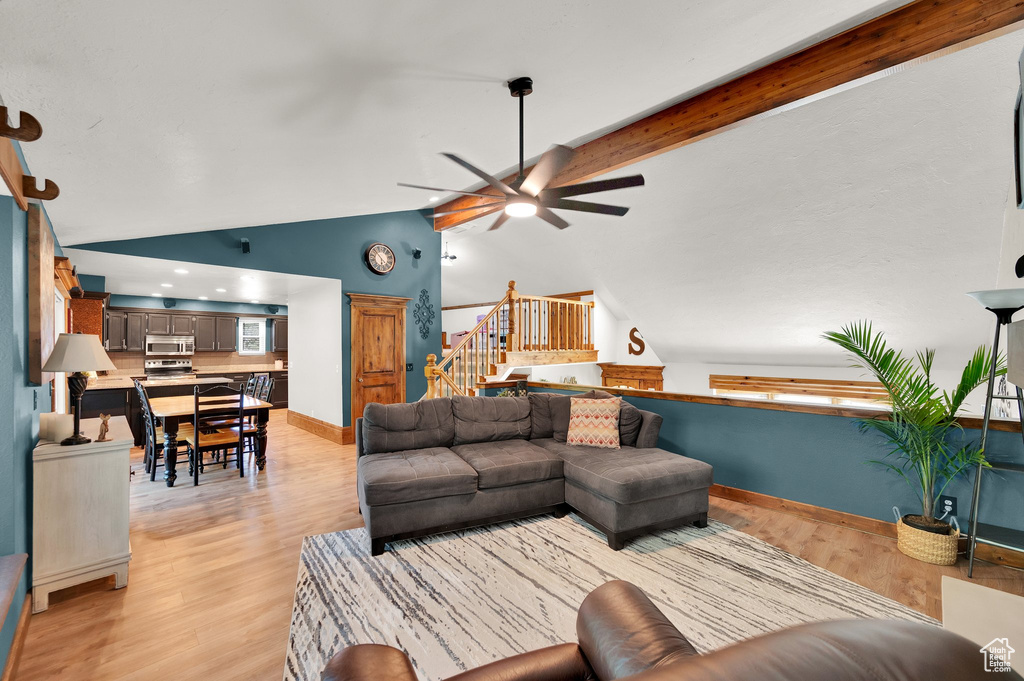 Living room with a ceiling fan, stairs, light wood-style floors, baseboards, and beamed ceiling