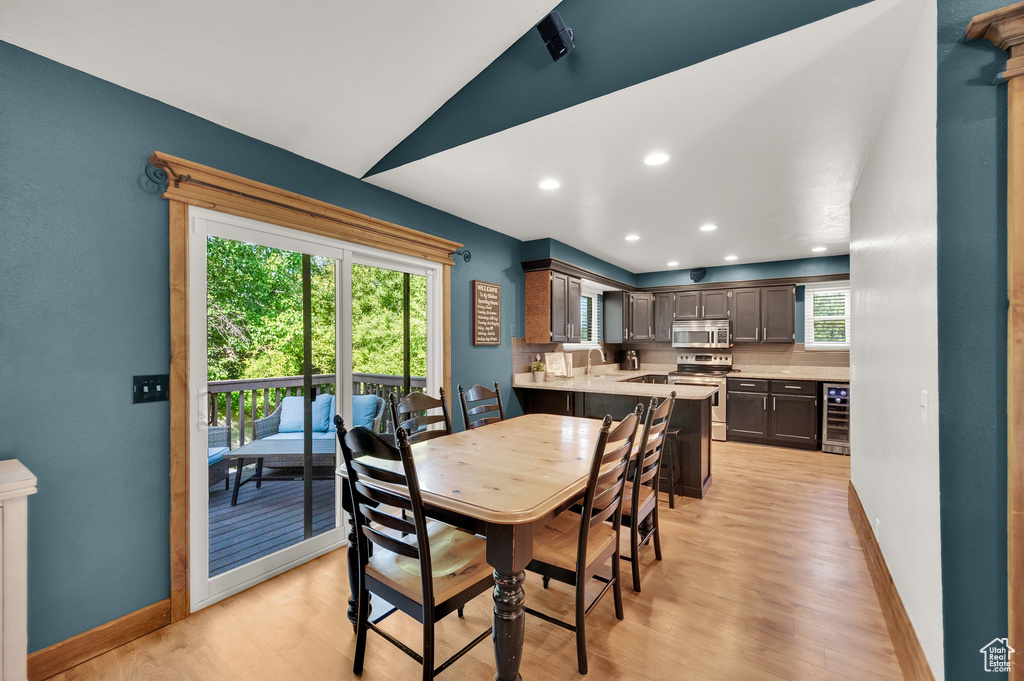Dining space with beverage cooler, light wood-style flooring, baseboards, lofted ceiling, and recessed lighting