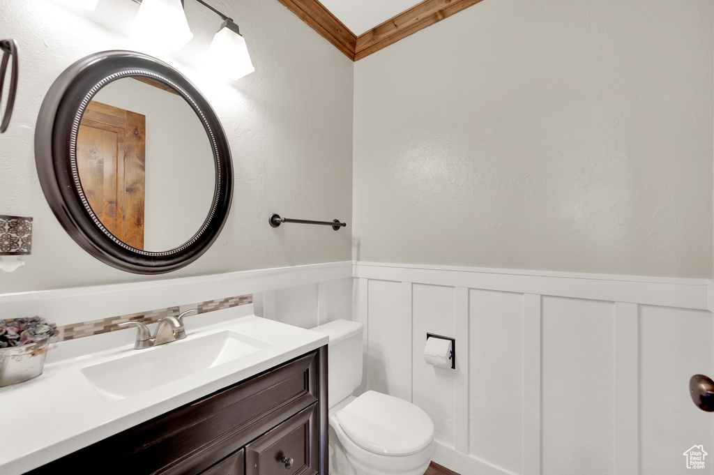 Bathroom featuring toilet, a wainscoted wall, vanity, a decorative wall, and ornamental molding