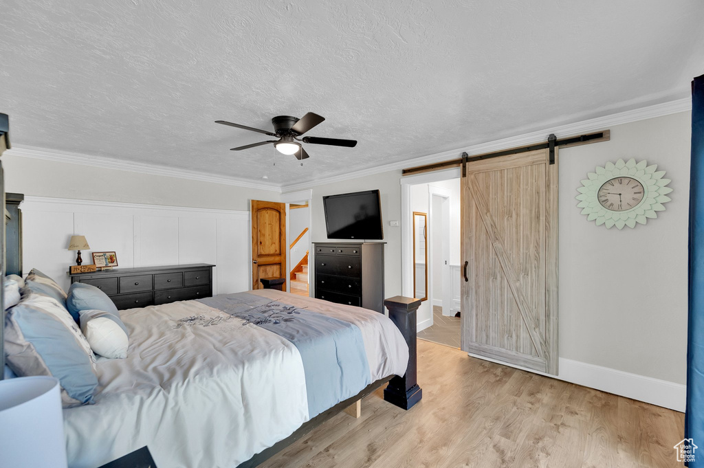 Bedroom featuring a barn door, ornamental molding, light wood finished floors, a ceiling fan, and baseboards