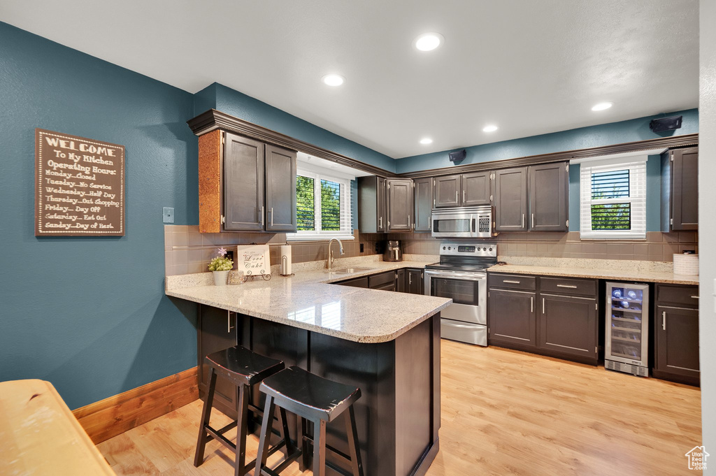 Kitchen with stainless steel appliances, wine cooler, a sink, a peninsula, and tasteful backsplash