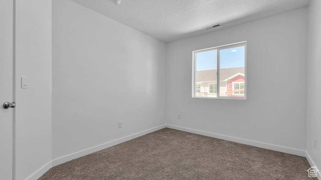 Empty room with dark carpet, baseboards, and a textured ceiling