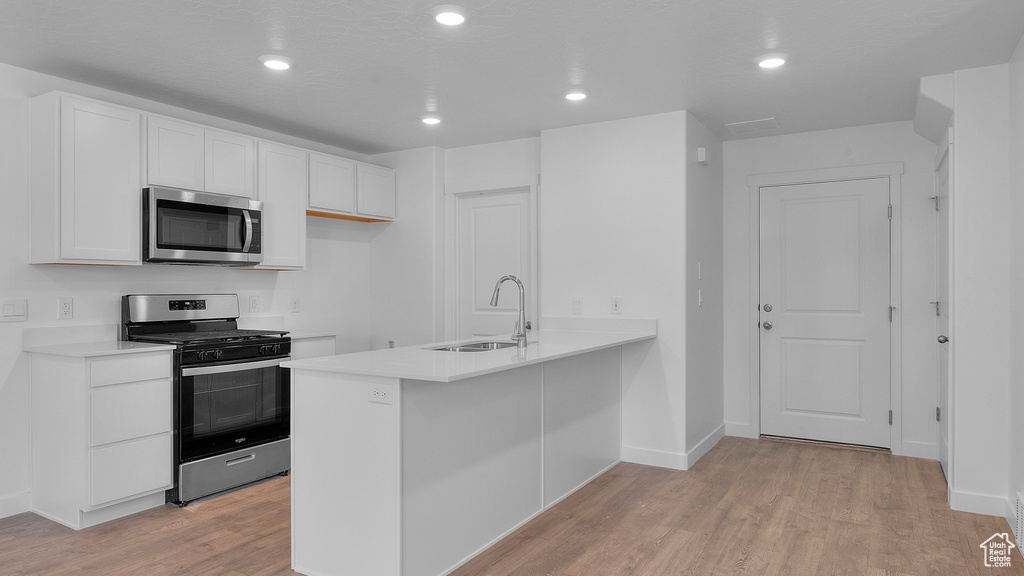 Kitchen with appliances with stainless steel finishes, a sink, light wood-style floors, white cabinets, and a peninsula