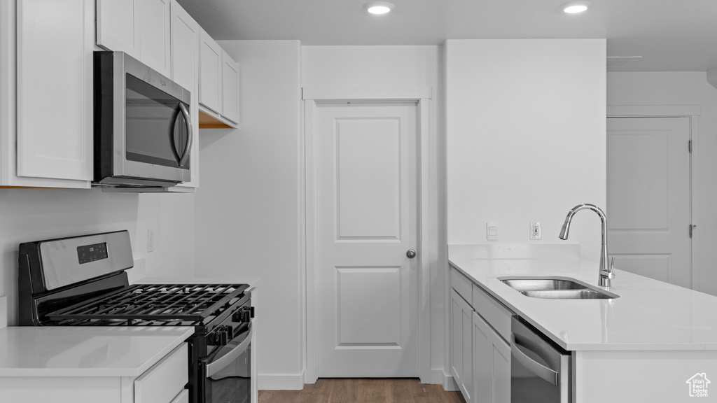Kitchen featuring stainless steel appliances, a sink, a peninsula, light wood-style flooring, and white cabinets