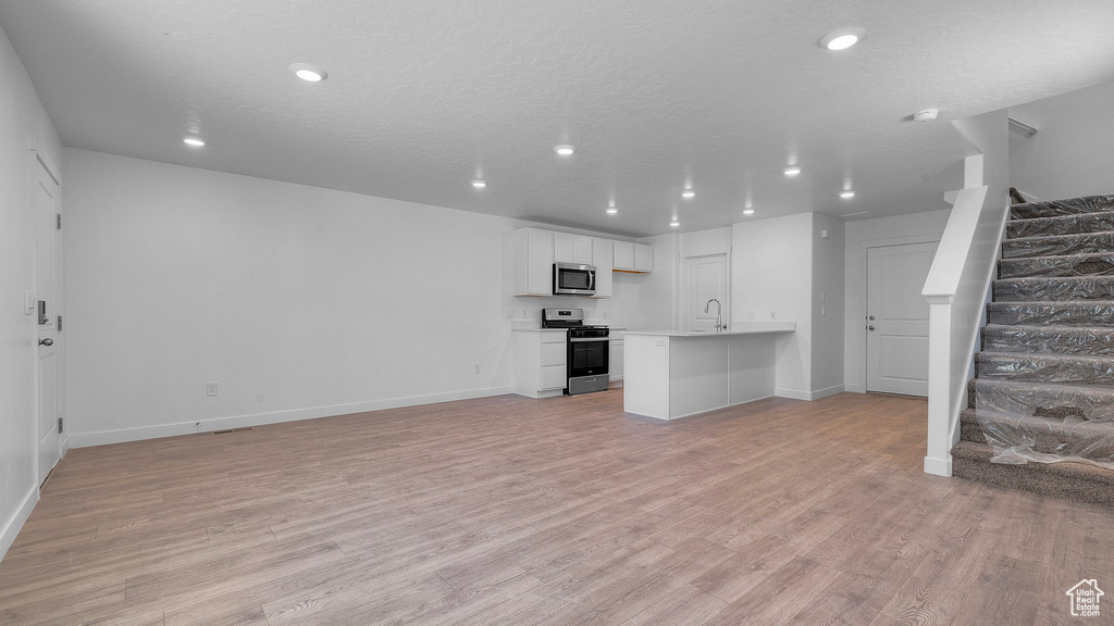 Unfurnished living room with stairs, light wood-style flooring, baseboards, and recessed lighting