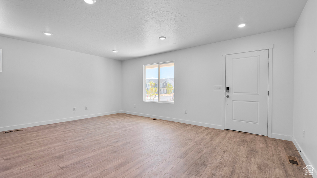 Empty room with light wood-style floors, recessed lighting, baseboards, and a textured ceiling