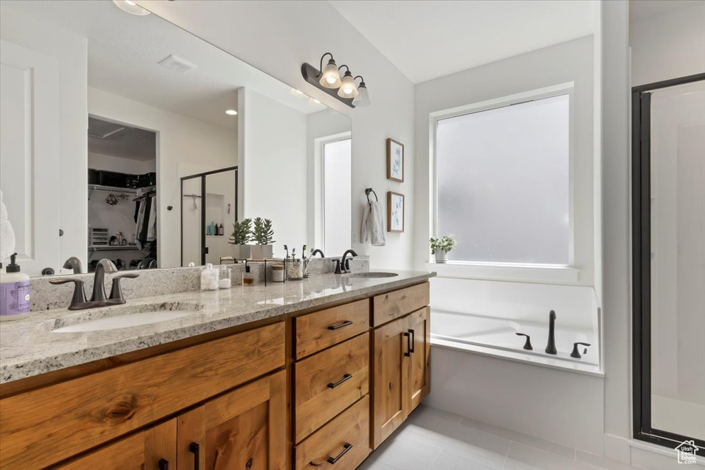Full bath featuring a stall shower, double vanity, a walk in closet, a garden tub, and tile patterned flooring