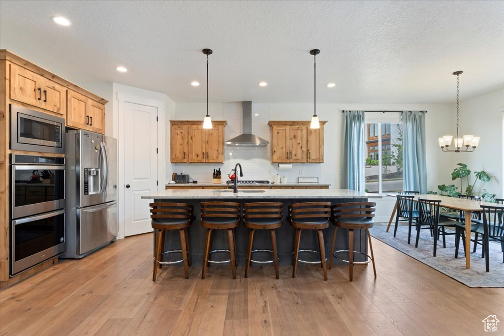 Kitchen with wall chimney range hood, stainless steel appliances, light wood-type flooring, decorative backsplash, and a kitchen breakfast bar