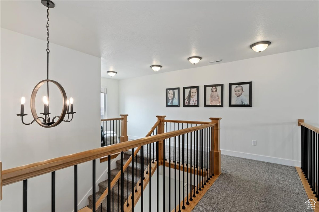 Corridor with an upstairs landing, a chandelier, baseboards, and carpet floors