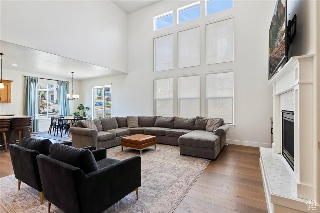 Living room featuring a fireplace with raised hearth, a high ceiling, hardwood / wood-style floors, a chandelier, and baseboards