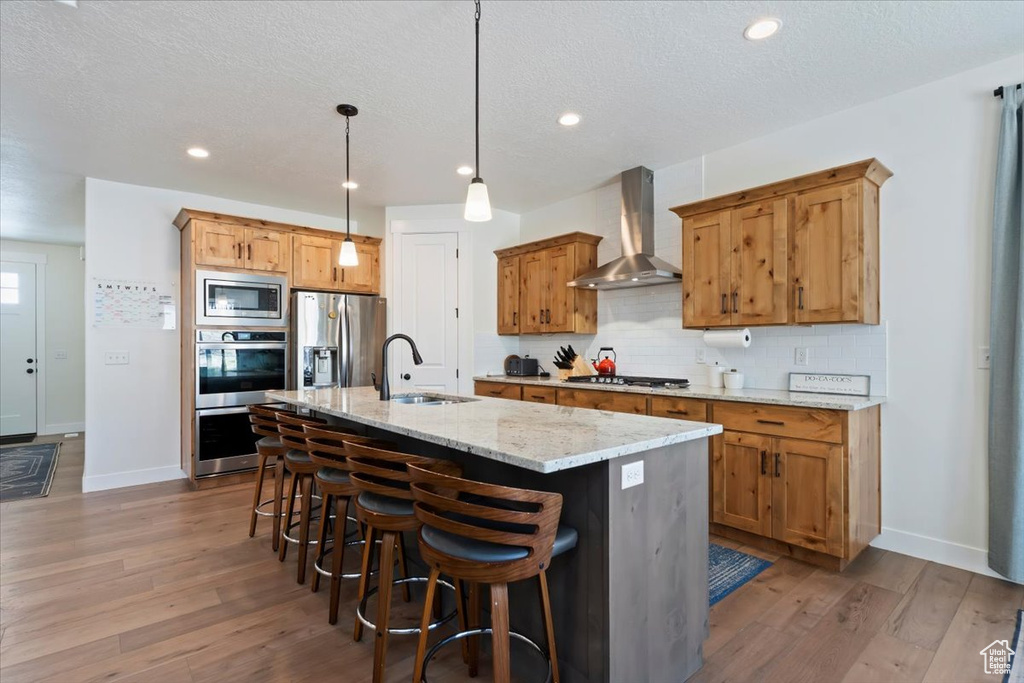 Kitchen featuring wall chimney exhaust hood, a sink, stainless steel appliances, baseboards, and tasteful backsplash