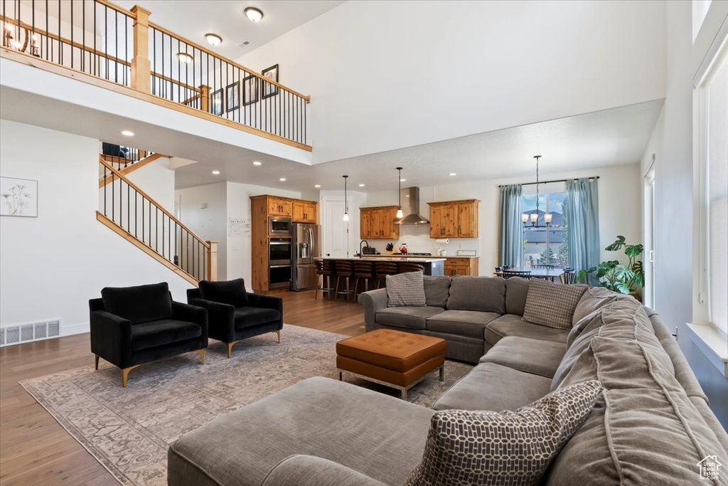 Living area with a towering ceiling, light wood-style floors, stairs, a chandelier, and recessed lighting