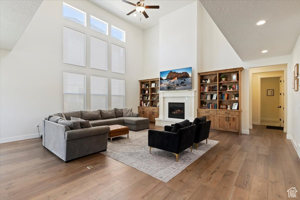 Living area featuring ceiling fan, a high ceiling, light wood finished floors, a fireplace with raised hearth, and baseboards