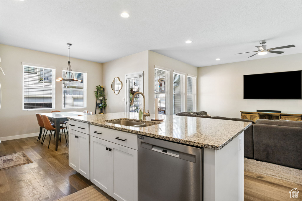 Kitchen featuring stainless steel dishwasher, a sink, open floor plan, dark wood-style floors, and light stone countertops