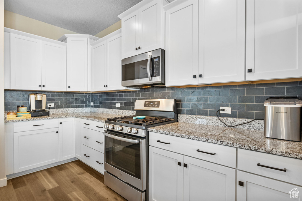 Kitchen with stainless steel appliances, light wood-style floors, white cabinets, decorative backsplash, and light stone countertops