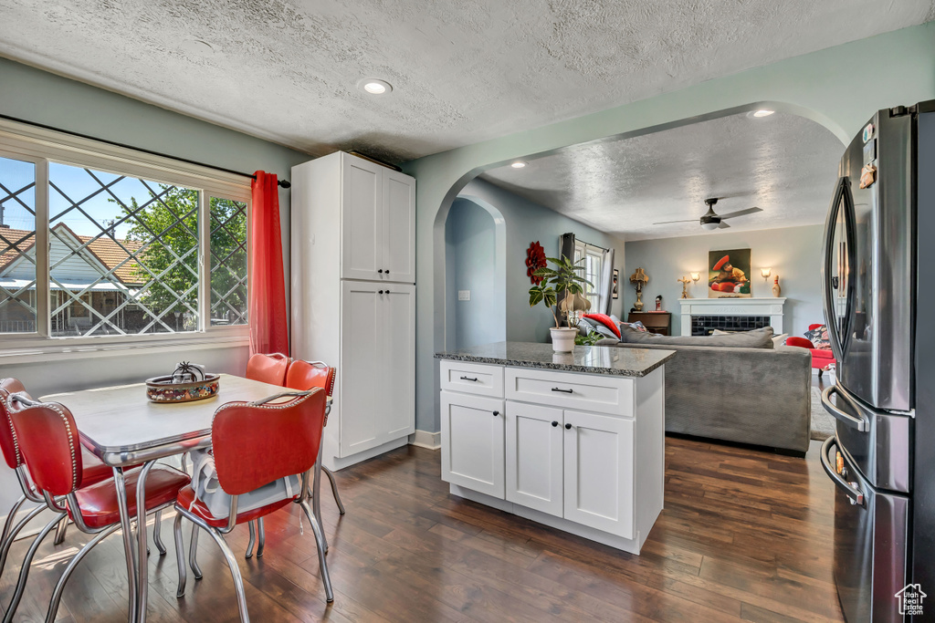 Kitchen with freestanding refrigerator, a textured ceiling, arched walkways, a ceiling fan, and dark wood-style flooring