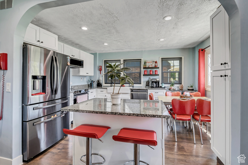 Kitchen featuring appliances with stainless steel finishes, arched walkways, dark wood finished floors, a textured ceiling, and white cabinets