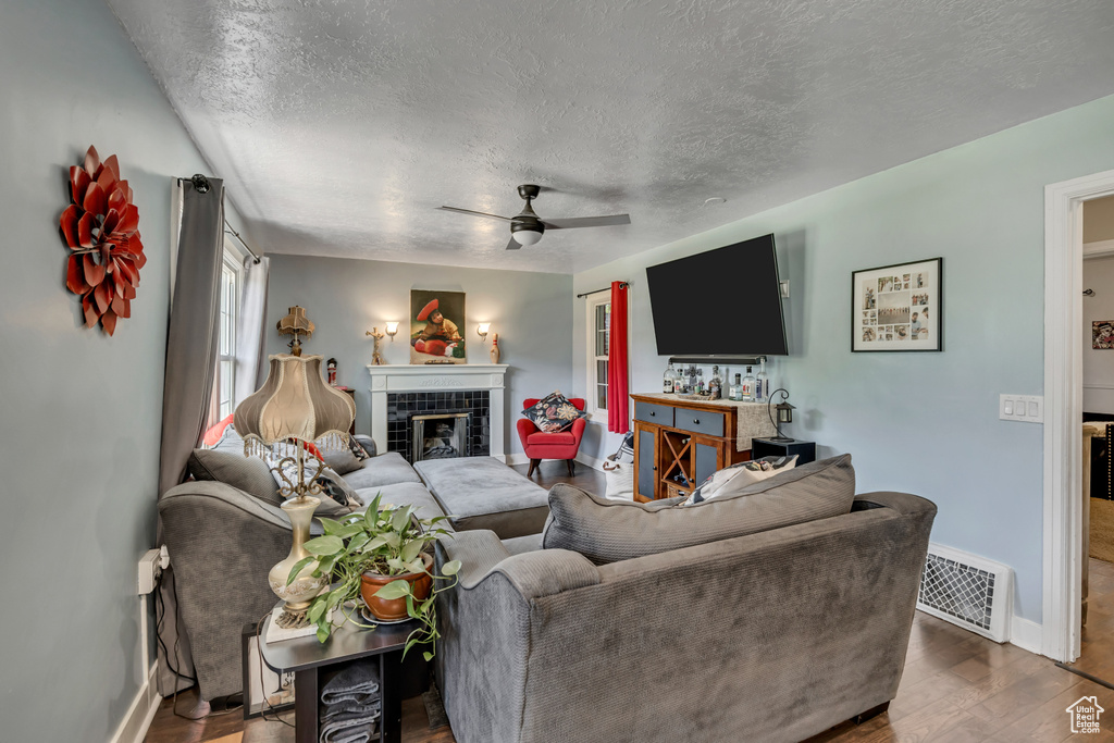 Living room with a textured ceiling, baseboards, wood finished floors, ceiling fan, and a tile fireplace