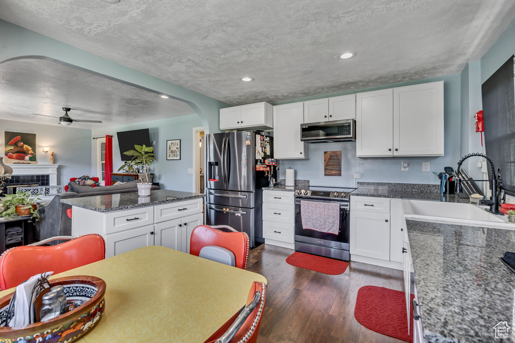 Kitchen with stainless steel appliances, a sink, arched walkways, dark wood-type flooring, and white cabinetry