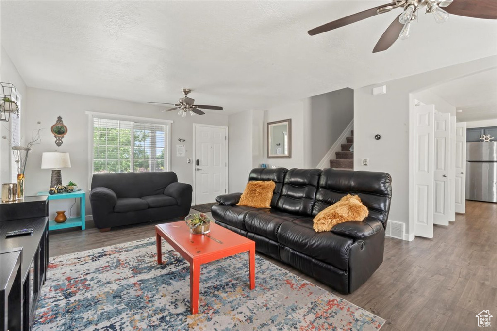 Living area with a ceiling fan, wood finished floors, stairs, and baseboards