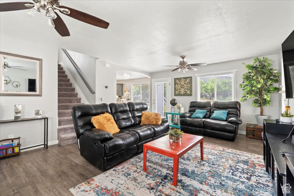 Living room with a ceiling fan, wood finished floors, healthy amount of natural light, stairs, and a textured ceiling