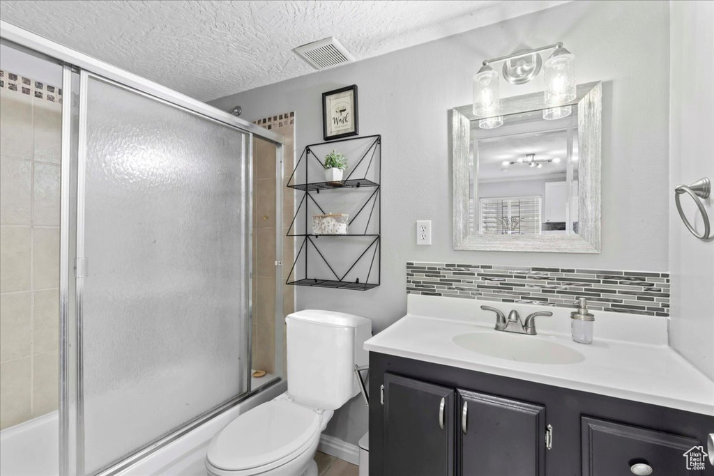 Full bathroom featuring vanity, toilet, decorative backsplash, shower / bath combination with glass door, and a textured ceiling