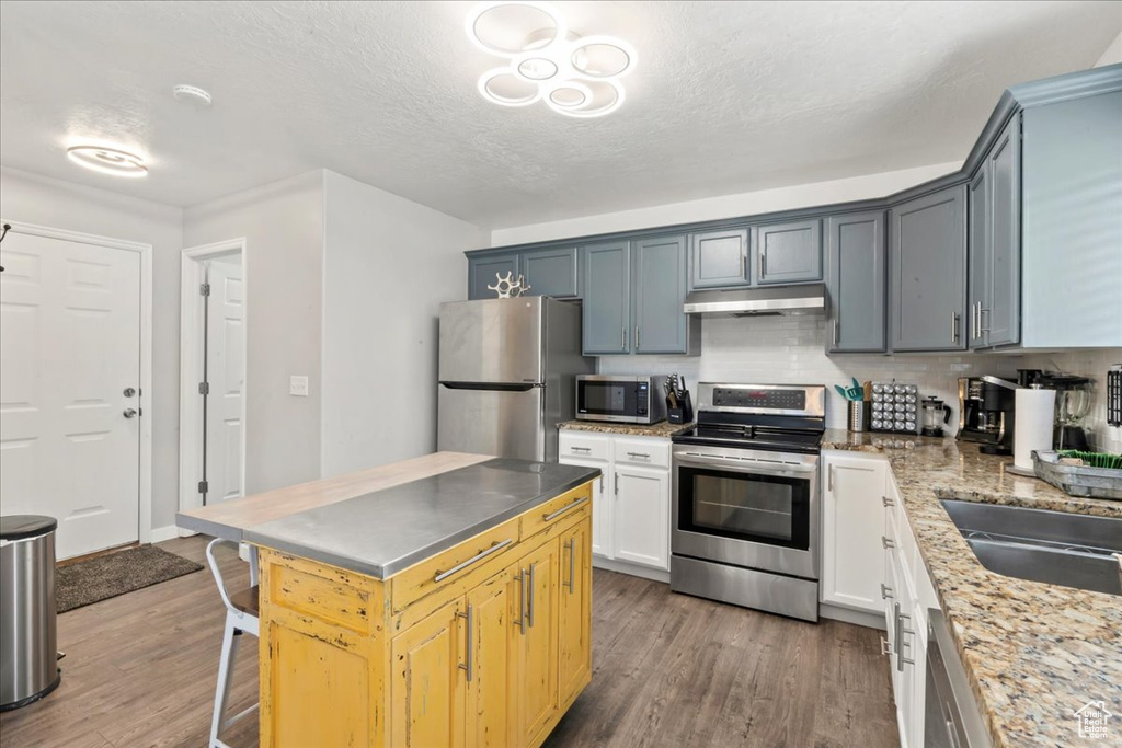 Kitchen featuring appliances with stainless steel finishes, under cabinet range hood, wood finished floors, decorative backsplash, and a kitchen breakfast bar