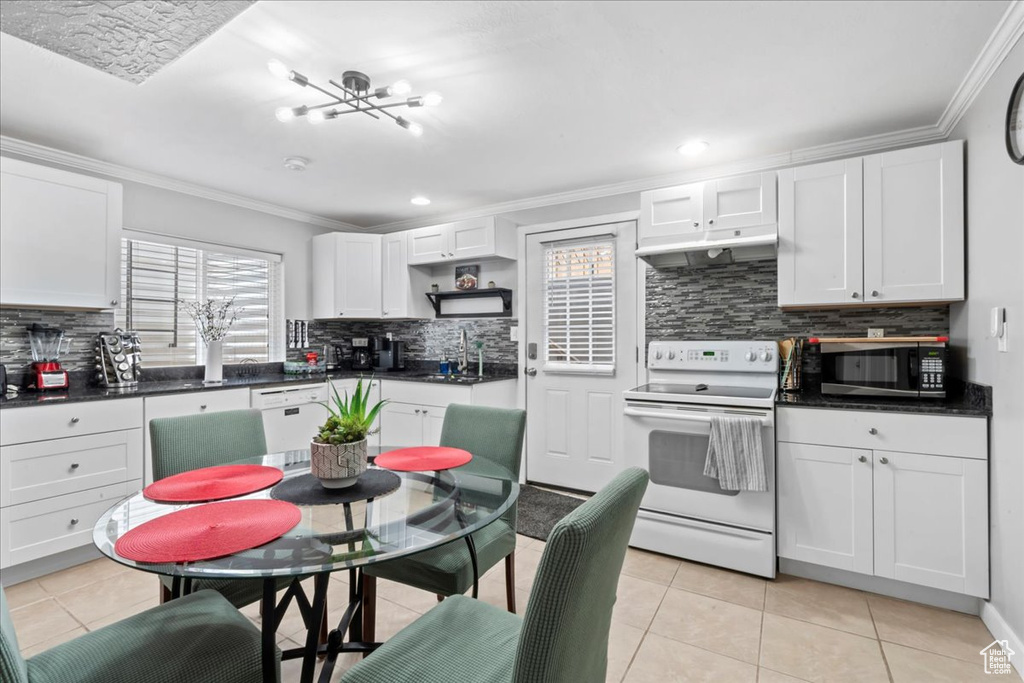 Kitchen featuring white appliances, under cabinet range hood, backsplash, ornamental molding, and light tile patterned floors