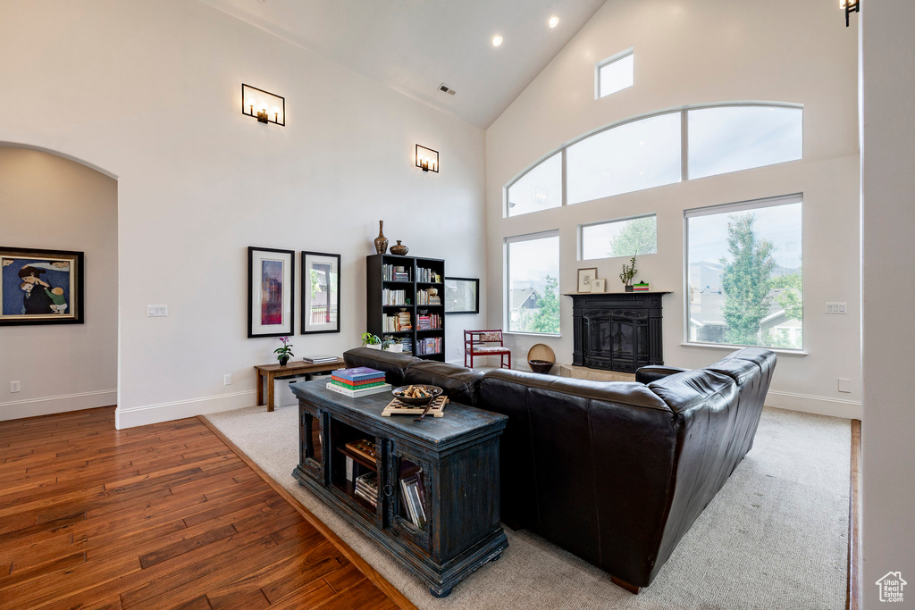 Living room featuring high vaulted ceiling, light wood finished floors, recessed lighting, a fireplace with raised hearth, and baseboards
