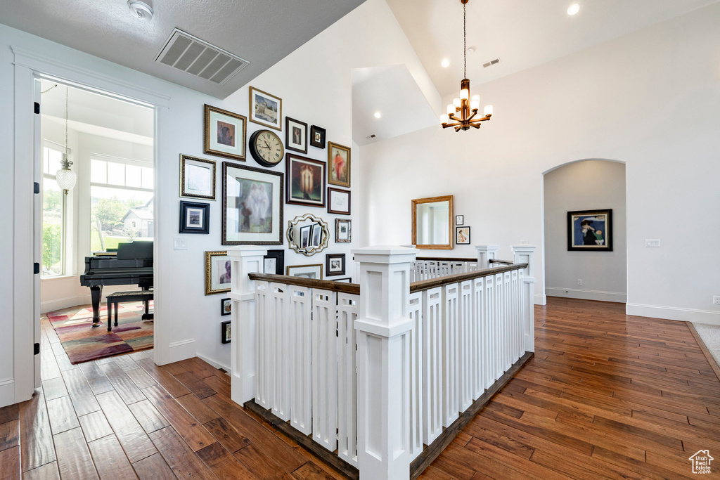 Corridor with a chandelier, dark wood-type flooring, an upstairs landing, baseboards, and arched walkways