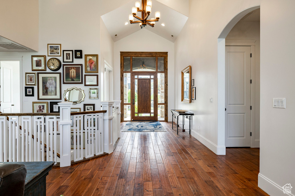 Foyer with high vaulted ceiling, arched walkways, hardwood / wood-style flooring, a chandelier, and baseboards