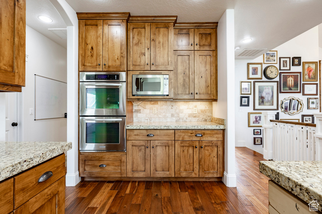 Kitchen with stainless steel appliances, tasteful backsplash, dark wood-style floors, and brown cabinetry