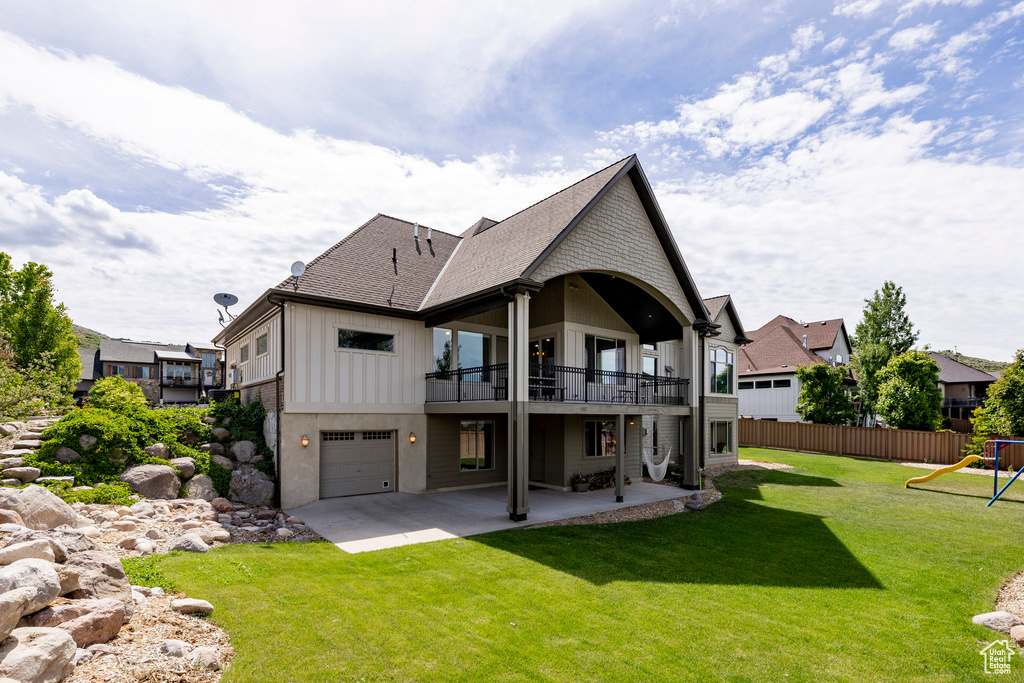 Rear view of property with a patio area, a balcony, roof with shingles, a garage, and a playground