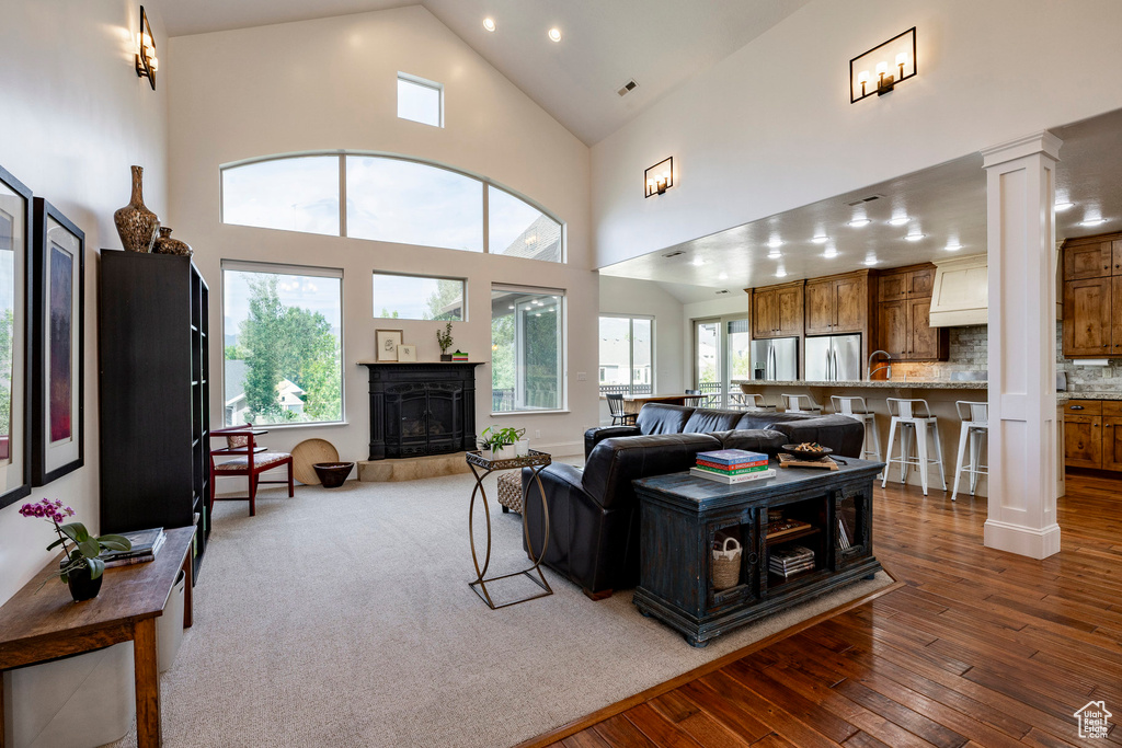Living room featuring wood-type flooring, decorative columns, high vaulted ceiling, plenty of natural light, and a fireplace with raised hearth