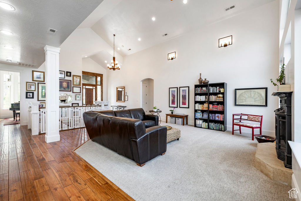 Living area with high vaulted ceiling, arched walkways, decorative columns, hardwood / wood-style floors, and recessed lighting